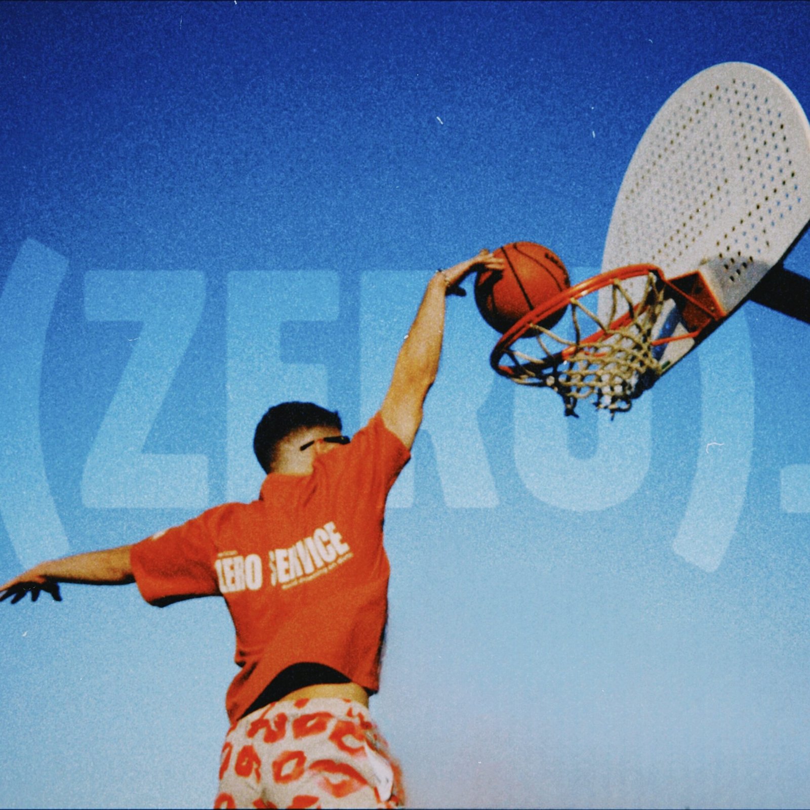 Persona haciendo un mate en una cancha de baloncesto al atardecer, vistiendo una camiseta roja de (zero). con el mensaje 'zero service', sobre un fondo con el logo de la marca. Imagen que representa fuerza, expresión y conciencia social a través de la moda.